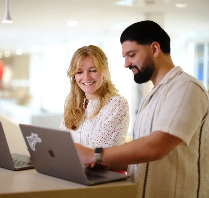 Two employees who explain each other something standing in front of their laptops as they point to the screen